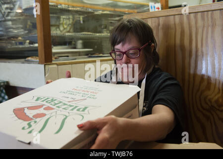 Marietta, GA, Stati Uniti d'America. 19 giugno 2019. Kathleen Gruen, 56, piega le scatole per prendere-out pizza in un piccolo ristorante italiano. Gruen, che ha la sindrome di Down, un disordine genetico, ha lavorato lo stesso supportato-occupazione lavoro per dodici anni, 2 giorni a settimana. Il lavoro aiuta a conservare la sua indipendenza, vive con due compagni di stanza in un supportati appartamento vivente. Ella ha sostegno da parte di personale addestrato e finanziato dalla sua rinuncia Medicaid. Credito: Robin Rayne/ZUMA filo/Alamy Live News Foto Stock