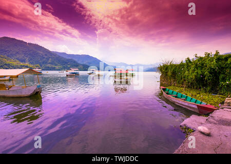 Colorate barche a pedali parcheggiato nel lago Phewa, blue hills e nuvole al tramonto sullo sfondo Pokhara Nepal. Foto Stock