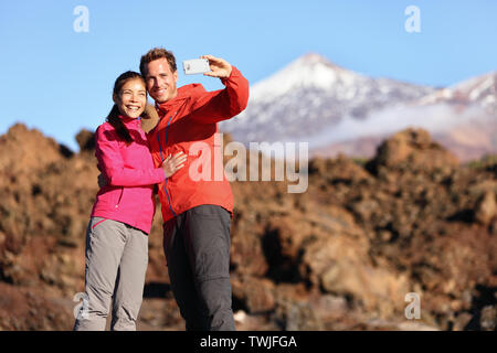 Giovane tenendo selfie escursioni nella splendida natura con smart phone. Coppia felice passeggiate godendo di vista e scattare foto con lo smartphone. L uomo e la donna dal vulcano Teide Tenerife, Isole Canarie. Foto Stock