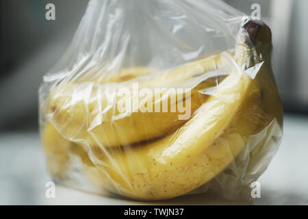 Un mazzetto di quasi banane mature avvolto in una sacca di plastica trasparente di colore bianco sulla superficie del tavolo Foto Stock