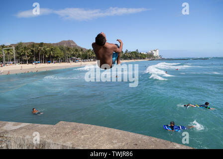 Un giovane maschio persona salta dal bordo e retro capovolge in acqua verso il basso al di sotto del Waikiki Beach, Hawaii. Foto Stock