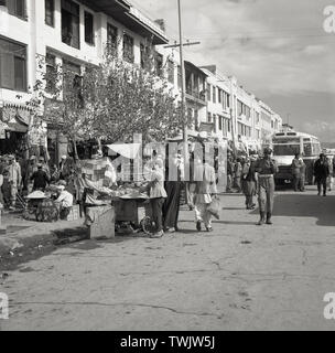 Degli anni Cinquanta, foto storiche di questa epoca, mostrando bustingly attività in una strada o una strada transitabile a Kabul, Afghanistan, con bancarelle, persone shopers, bus e poliziotto afghano. Foto Stock