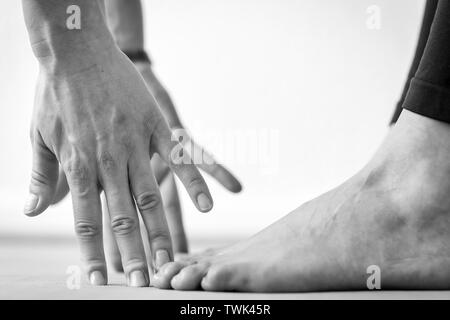 Close-up vista laterale delle mani e dei piedi di una giovane donna pratica Uttanasana o permanente di piegare in avanti lo Yoga posa, vista orizzontale Foto Stock