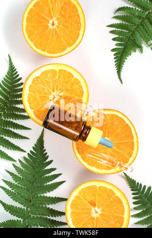 Olio essenziale di agrumi, vitamina c siero con fresche succosa frutta di arancia e foglia di felce su sfondo bianco. Organici cosmetici spa con ingredienti a base di erbe per Foto Stock