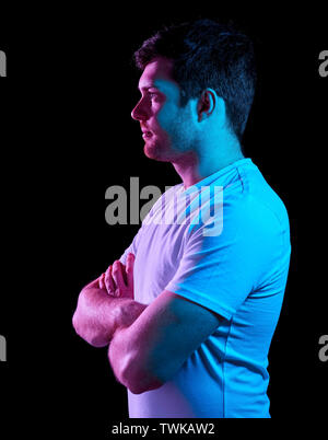 Uomo con bracci incrociati su luci al neon nelle tenebre Foto Stock
