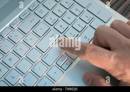 L'uomo la mano sulla tastiera del notebook su uno sfondo luminoso. guy preme il pulsante Invio sulla tastiera grigio della moderna ultrabook. Foto Stock