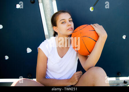 Femmina giovane giocatore di basket con impegnativo volto seduto sul pavimento Foto Stock