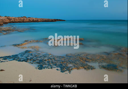 Vista di sabbia vuota sterile Poseidon spiaggia nei pressi di ayia napa, Cyrpus. Cielo blu al di sopra di acqua poco profonda con barriere coralline. Serata calda in caduta. Copia dello spazio. Lunga expo Foto Stock