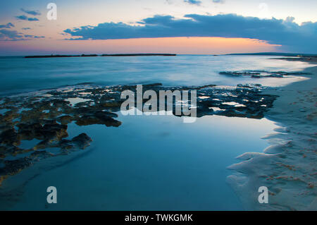 Vista del vuoto Poseidon sabbiosa spiaggia nei pressi di ayia napa, Cyrpus. Tramonto cielo arancione, grigio sopra le nuvole blu scuro acqua poco profonda, impronte, barriere coralline. Calda anche Foto Stock