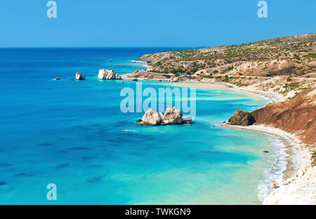 Vista da sopra su Petra tou Romiou mare pietra miliare dello stack nei pressi di Afrodite, Luogo di nascita di Paphos, Cipro. Spruzzi delle onde contro la spiaggia di scuro e rosso collina. W Foto Stock