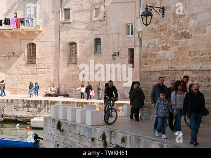 Monopoli,Italia;due ciclisti sul molo del vecchio porto di pesca della città di Monopoli,su una domenica mattina di primavera mentre in bicicletta tra la folla. Foto Stock