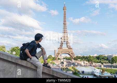 Un uomo con zaino guardando la torre Eiffel, famoso punto di riferimento e meta di viaggio a Parigi, Francia. Viaggiare in Europa in estate Foto Stock