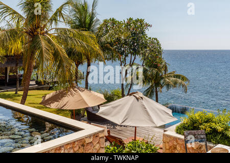 Lettini da sole con ombrelloni vicino a una piscina con vista oceano, Amed, Karangasem Regency, Bali, Indonesia. Foto Stock