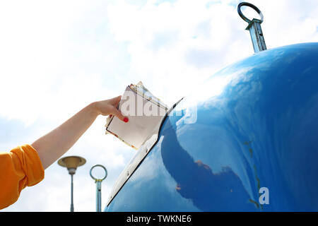 Riciclaggio di una donna getta lo spreco di carta in un contenitore blu Foto Stock