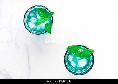 Due belle vintage occhiali turchese con bevanda fredda e cubetti di ghiaccio, decorata con fresco verde menta su marmo bianco tavola. Vista dall'alto. Foto Stock