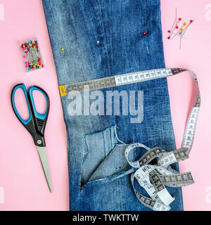 Piegate a metà jeans blu con un grande foro sulla gamba pant, multi colore cucitura testa perni, bianco nastro su misura con centimetri e pollici e forbici. Foto Stock