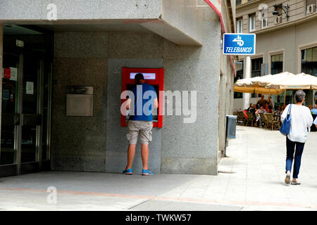 Giovane uomo utilizzando un Bancomat presso una banca Santander succursale in Granada, Spagna; Telebanco. Foto Stock