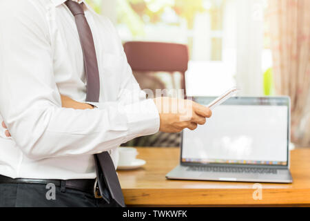 Businessmans mano azienda cellulare con il laptop sulla scrivania in legno. Foto Stock