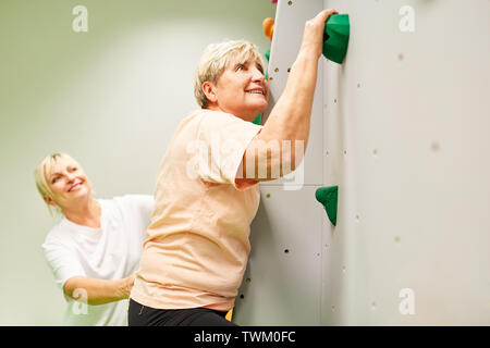 Fisioterapista dà senior donna assistenza in arrampicata su una parete di arrampicata Foto Stock