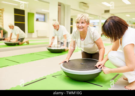 Fisioterapista aiuta donna senior con un allenamento fitness con il Bosu palla in palestra Foto Stock