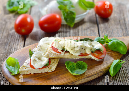 Panini al forno caprese con pomodoro, mozzarella e basilico, servita su un tagliere di legno Foto Stock