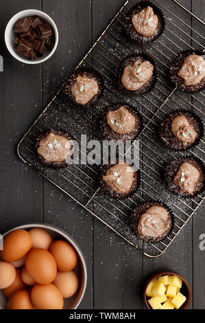 Torte di Fairy su un vassoio di raffreddamento con una spolverata di zucchero a velo e gli ingredienti, su un invecchiato in legno grigio Sfondo, ripresa dall'alto Foto Stock