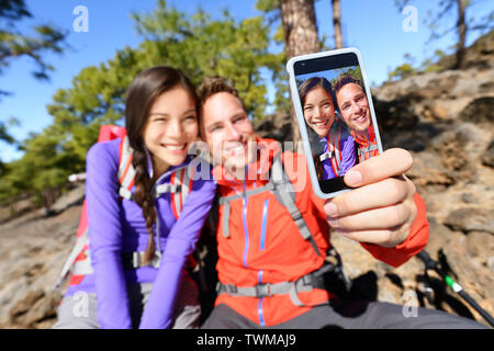 Selfie giovane utilizzando smart phone gite nella natura con lo smartphone. Coppia felice tenendo Self-portrait foto utilizzando l'app. L uomo e la donna per divertirsi insieme. Focus sullo schermo. Foto Stock