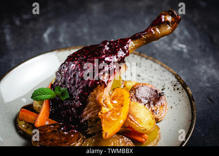 Grasso di arrosto di oca gamba con patate, carote e arance Foto Stock