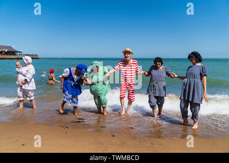 Broadstairs Dickens Festival. Cinque senior, uomo e donna, vestito in stile vittoriano costumi da bagno, tenendo le mani, ridendo e rivolta verso il visualizzatore, in piedi paddling in mare al Viking Bay Beach. Sole brillante. Foto Stock