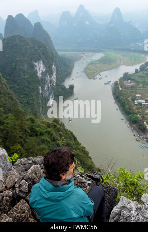 L'uomo oltre il Fiume Li e il paesaggio carsico sulla cima di una collina in Xingping, provincia di Guangxi, Cina Foto Stock