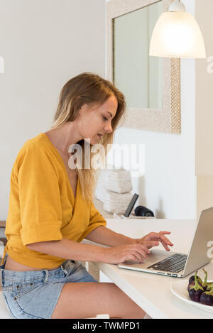 Ragazza che lavora utilizzando il portatile in cucina Foto Stock