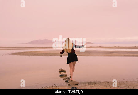 Vista sul retro di una giovane donna con capelli lunghi biondi come lei si affaccia la vasta scena del grande lago salato a distanza, Foto Stock