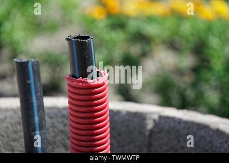 Il cavo di comunicazione all'aperto, la posa di un cavo in fibra ottica per internet veloce, elettricità e cavo telefonico lungo una nuova strada. Installazione dei cavi di potenza Foto Stock