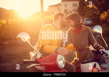Amare giovane coppia in scooter godendo in viaggio sulla strada romantica in vacanza al tramonto. Foto Stock