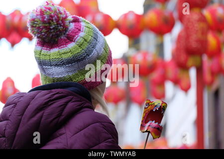 Una ragazza siede sulle spalle di un genitore che gioca con un leone di carta giocattolo a Chinatown con lanterne rosse sullo sfondo. Foto Stock