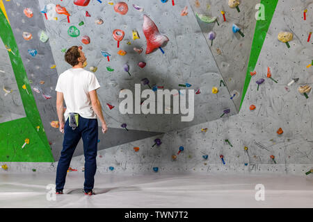 Rocciatore si alza e guarda la parete di arrampicata con ganci in boulder hall Foto Stock