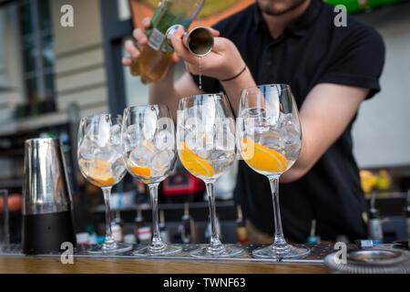 Quattro bicchieri in piedi sulla barra. Gli occhiali sono con ghiaccio e arancione. Barman versa alcool in bicchieri da un vetro di misurazione. Concetto di ristorante Foto Stock