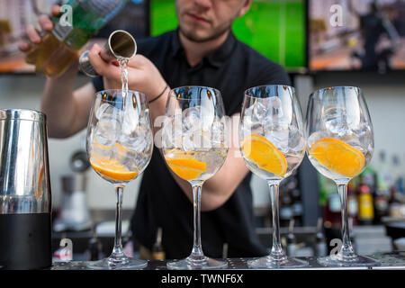Quattro bicchieri in piedi sulla barra. Gli occhiali sono con ghiaccio e arancione. Barman versa alcool in bicchieri da un vetro di misurazione. Concetto di ristorante Foto Stock