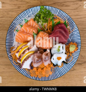 Piastra grande di sashimi, crudo e fresco tagliato a fette di pesce, calamari e polpi servita con carote e insalata verde, vista dall'alto Foto Stock