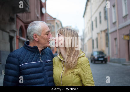 Ritratto di felice coppia romantica con differenza di età kissing all'aperto nella città antica in primavera o in autunno. Foto Stock