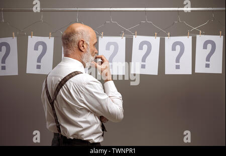 Malinconici uomo confrontare diverse possibilità e domande, fissando in molti punti interrogativi Foto Stock