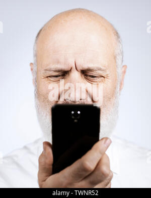 Senior uomo utilizzando le applicazioni sullo smartphone, egli sta avendo difficoltà e problemi di visione Foto Stock