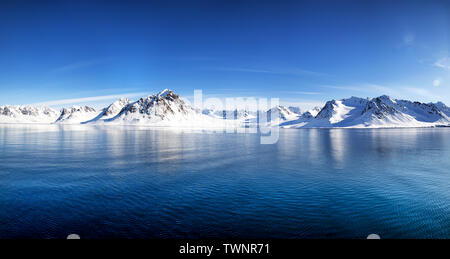 Cielo blu, blu e montagne innevate in splendidi fiordi delle Isole Svalbard, un arcipelago norvegese tra il continente Norvegia e il Polo Nord Foto Stock