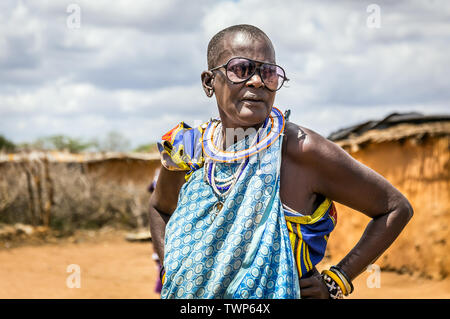 Villaggio dei masai, KENYA - 11 ottobre 2018: Unindentified senior africana donna che indossa gli abiti tradizionali e grandi bicchieri in tribù Masai, Kenya Foto Stock