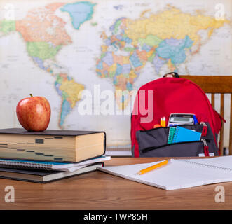 Aperto il notebook e pila di libri su una tabella con la scuola bookbag e la mappa del mondo in background Foto Stock