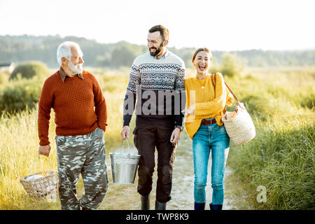 Giovane uomo e donna che cammina su un picnic con il senior nonno vestito di maglioni, la spesa di un buon tempo insieme sulla natura Foto Stock