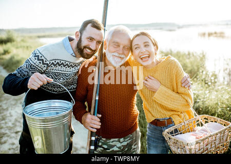 Ritratto di un giovane uomo e donna con allegro senior nonno abbracciando insieme all'aperto, aventi un buon tempo durante le operazioni di pesca Foto Stock