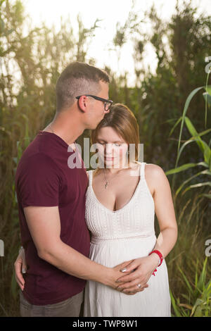 Amare luomo e felice donna incinta in un parco d'estate. Felice Coppia matura in amore abbracciando outdoor Foto Stock