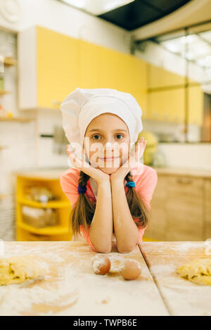 Bambina con grembiule e cappello del cuoco seduta nella cucina di casa.  Madre di helper. 2 anno di età Foto stock - Alamy