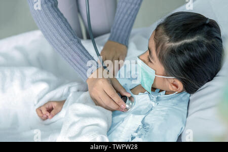 Medico guarire paziente asian kid sul letto di ospedale. Medicina situazione virus quando i bambini hanno la febbre alta. Medico usa uno stetoscopio per ascoltare polpa Foto Stock